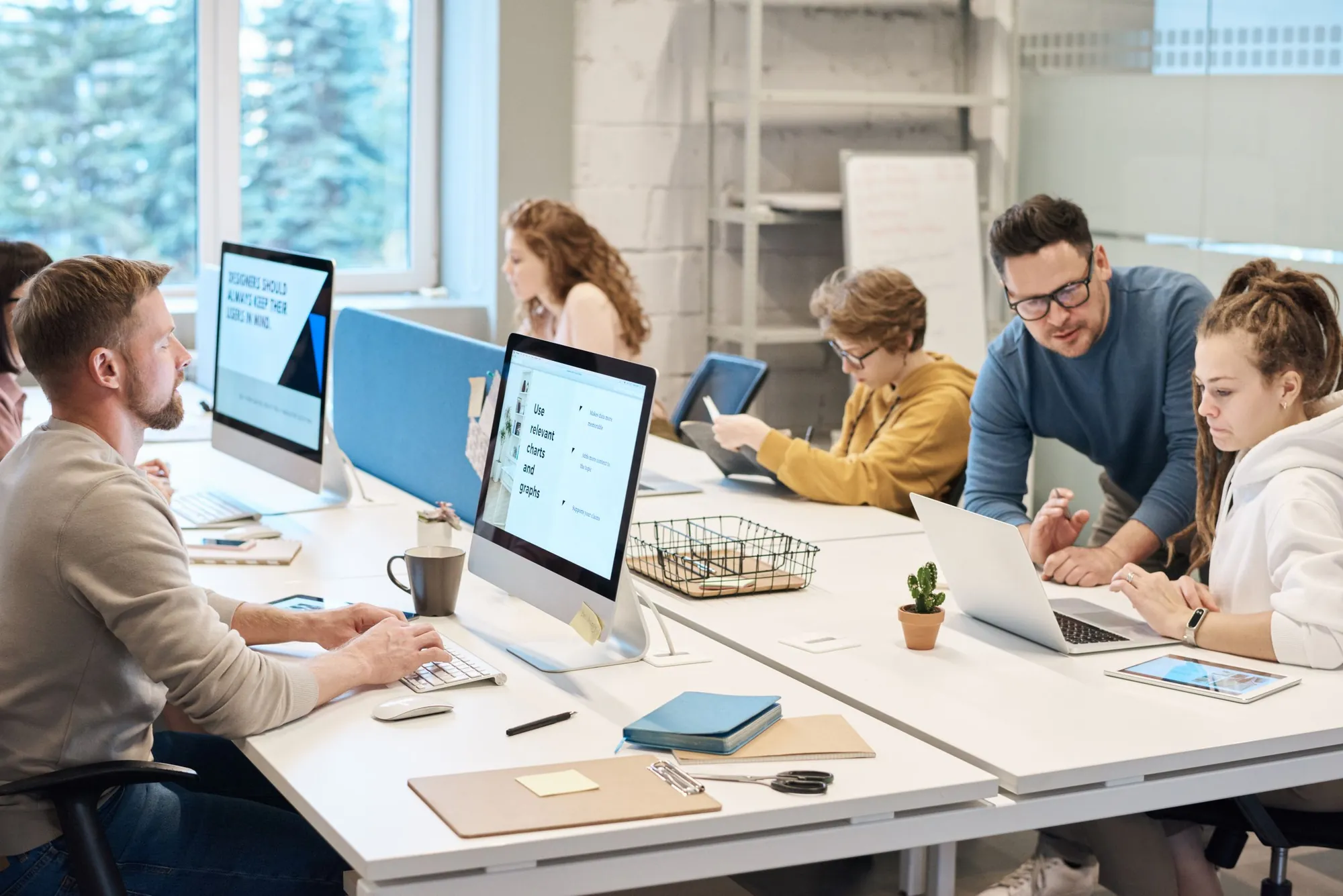 A software team working side by side at a shared desk, their screens showing dashboards and charts.